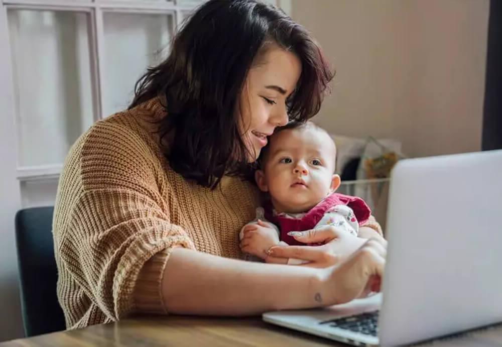 A multitasking mom holding her child, balancing work and family life