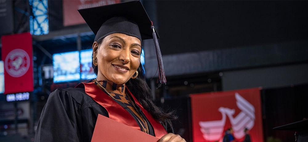 一位自豪地穿着毕业礼服的女士拿着毕业证书，这标志着她的教育成就